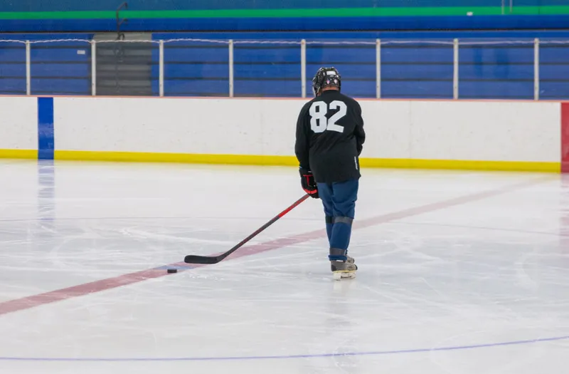 Hockey player wearing number 82 skates alone on an indoor rink with a stick and puck