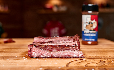 Sliced smoked brisket on a wooden cutting board with a spice rub bottle in the background