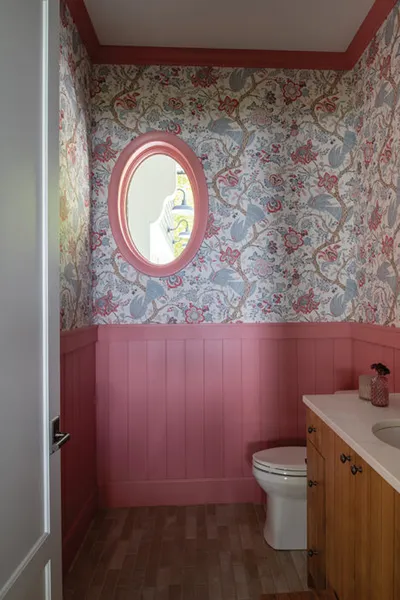 Powder room with floral wallpaper, pink wainscoting, oval pink-framed mirror, and wood vanity