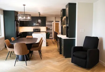 Open-concept kitchen and dining area with dark cabinetry, herringbone wood floors, and tan leather chairs