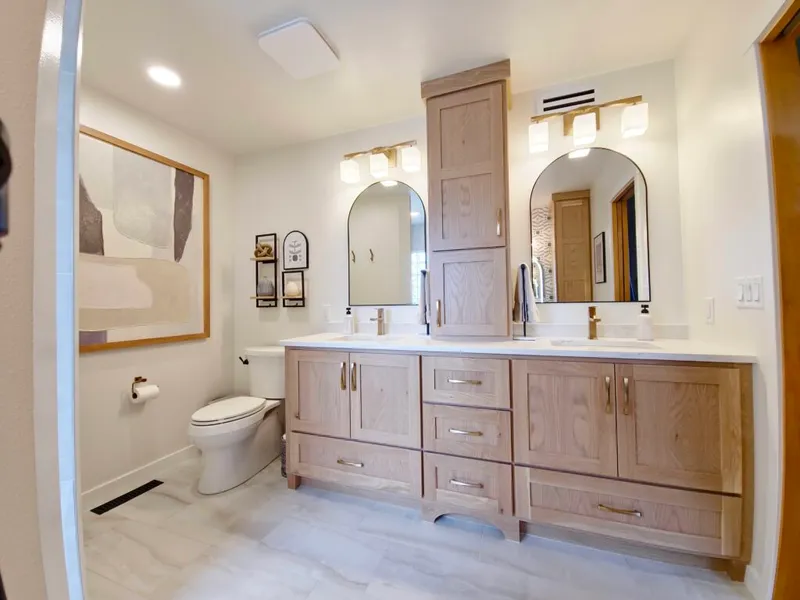 Remodeled bathroom with double wood vanity, arched mirrors, and tall center cabinet