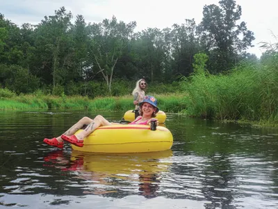Child relaxing in a yellow inflatable tube on a calm river, adult wading behind