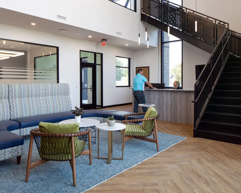 Modern office lobby with green chairs, blue sectional sofa, and a black metal staircase