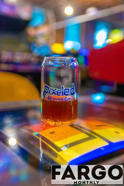 Pixeled Brewing Co. glass of amber beer on a colorful arcade game surface
