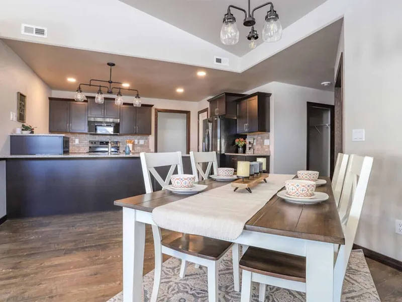 Open-concept dining area with wood table, white chairs, and dark-cabinet kitchen beyond