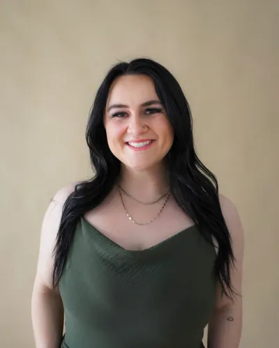 Smiling woman with long dark hair wearing a green tank top and layered necklaces