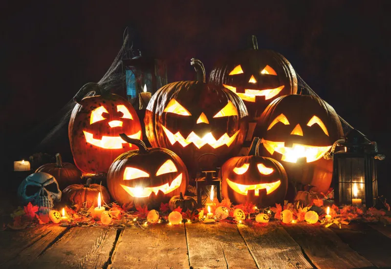 Glowing carved jack-o'-lanterns grouped on a wooden surface with candles, autumn leaves, and a skull