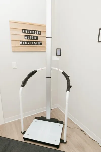 Medical body composition scale with support handles beside a 'Progress Weight Management' sign