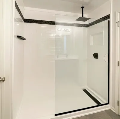 Walk-in shower with white walls, glass panel door, and matte black fixtures