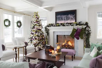 Holiday-decorated living room with flocked Christmas tree, lit fireplace, and green stockings on white mantel