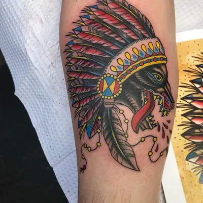 Colorful traditional tattoo of a snarling wolf wearing a feathered headdress on a forearm