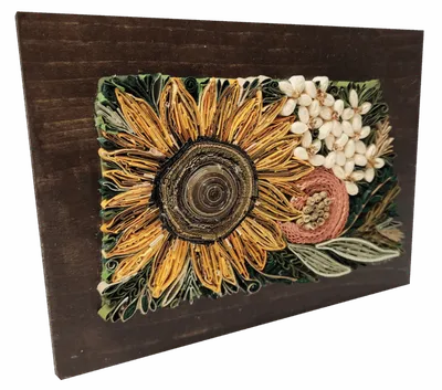 Paper quilling artwork of a sunflower with white blooms and a pumpkin on a dark wood frame