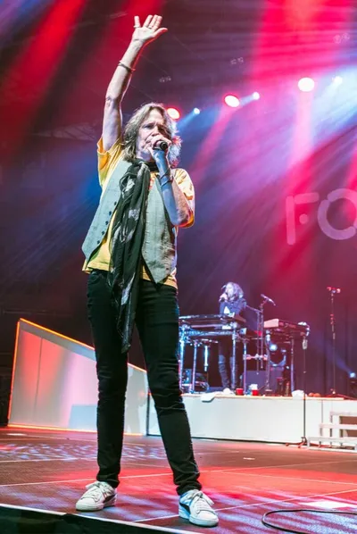 Male rock singer raising one hand to crowd on a lit concert stage