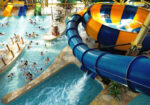Indoor waterpark with a blue spiral slide above a crowded wave pool