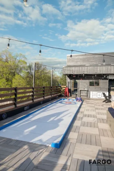 Outdoor deck with a synthetic curling lane, string lights, and a wood-sided building