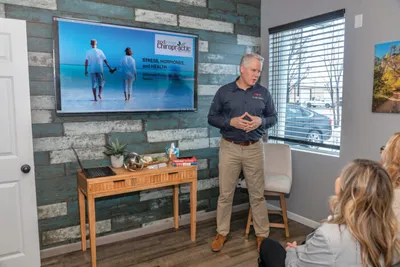 Man in dark shirt presents a wellness slideshow to seated attendees in a modern office