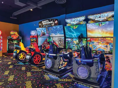 Arcade racing simulators including Top Gun Maverick and Fast & Furious cabinets in a colorful game room