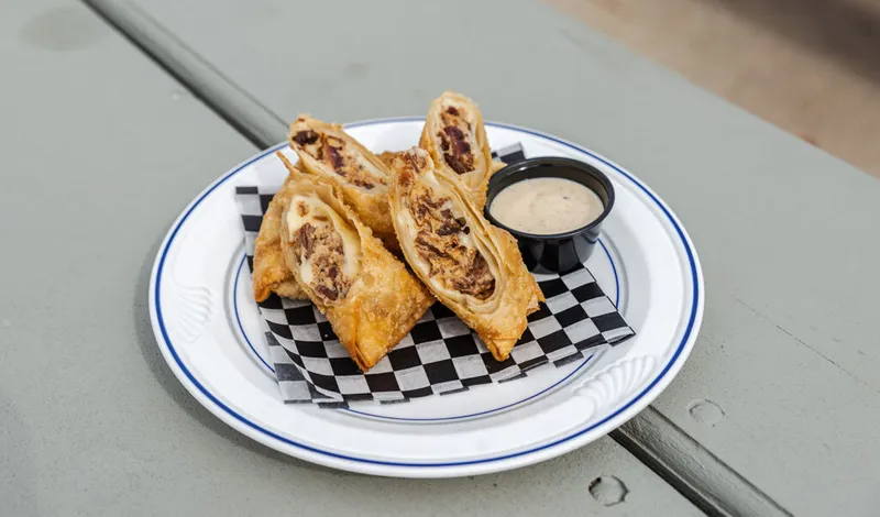 Fried egg rolls cut open to show meat filling, served with dipping sauce on a checkered liner