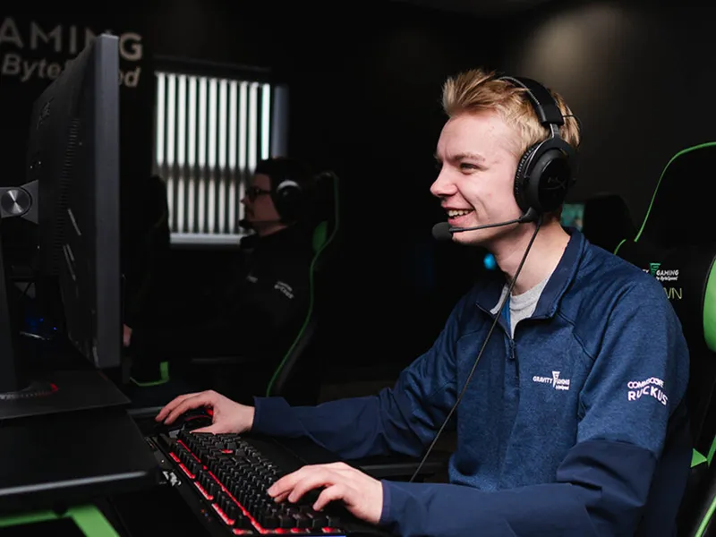 Smiling young man wearing a gaming headset plays at a PC in a dark esports setup
