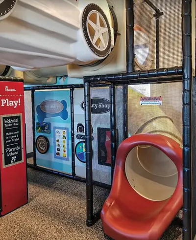 Indoor children's play area with a red tube slide, climbing structure, and themed activity panels