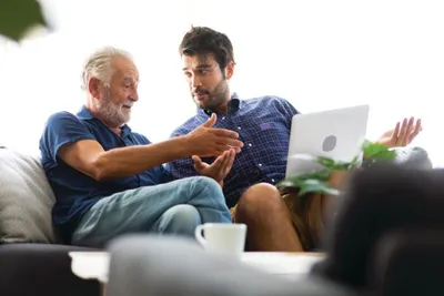 Older man and younger man reviewing a laptop together on a sofa