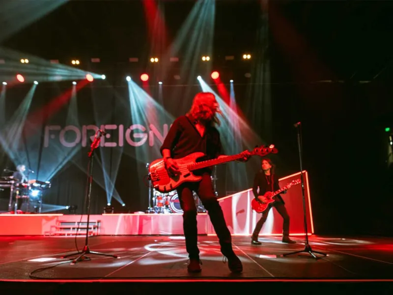 Foreigner guitarist performing on a red-lit stage with dramatic beam lighting