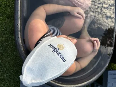 Person relaxing in an ice bath holding a white Moonglade branded mitt