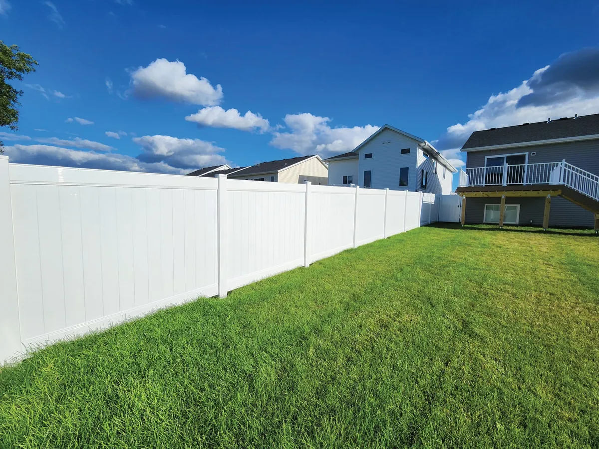 White vinyl privacy fence along a green suburban backyard with houses and deck behind