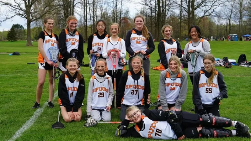 Youth girls lacrosse team in white and orange Spuds jerseys posing on a grass field