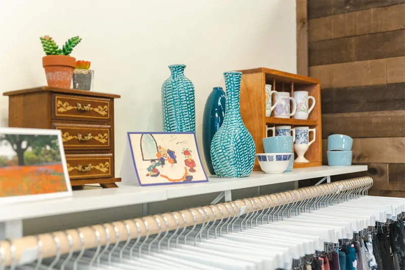 Teal ceramic vases, mugs, and bowls displayed on a shelf above clothing racks in a boutique