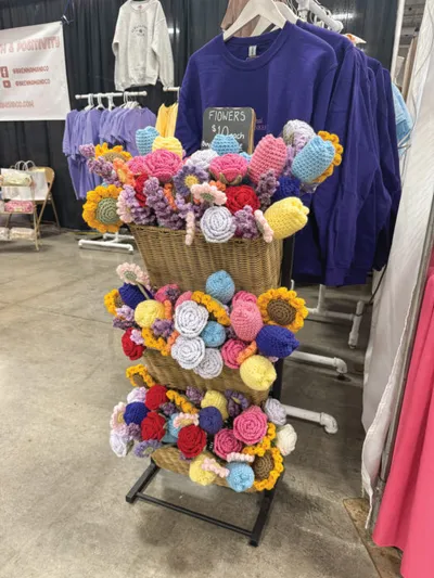 Tiered wicker basket display overflowing with colorful crocheted flowers at a craft market vendor booth