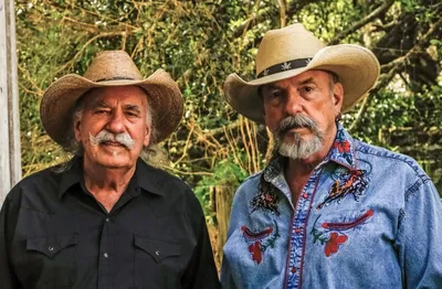 Two older men with mustaches and goatees wearing straw cowboy hats outdoors