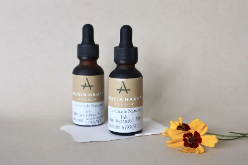 Two amber dropper bottles of Alicia Hauff Studio handmade natural ink beside yellow flowers