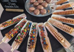 Wooden boat-shaped trays of colorful toppings arranged on a dark buffet table