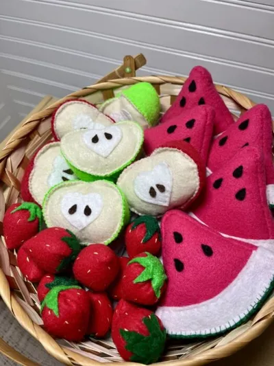 Wicker basket filled with handmade felt fruit including strawberries, apple slices, and watermelon wedges