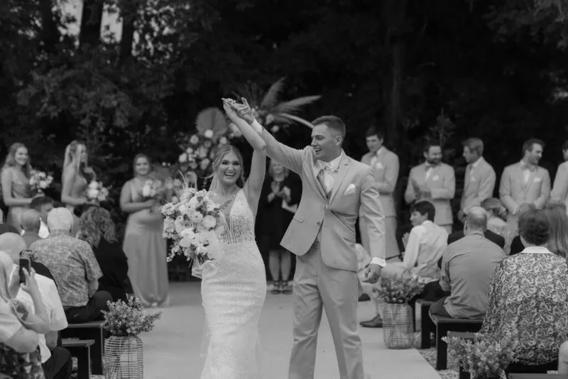 Bride and groom raising joined hands while walking back down the aisle at an outdoor wedding ceremony