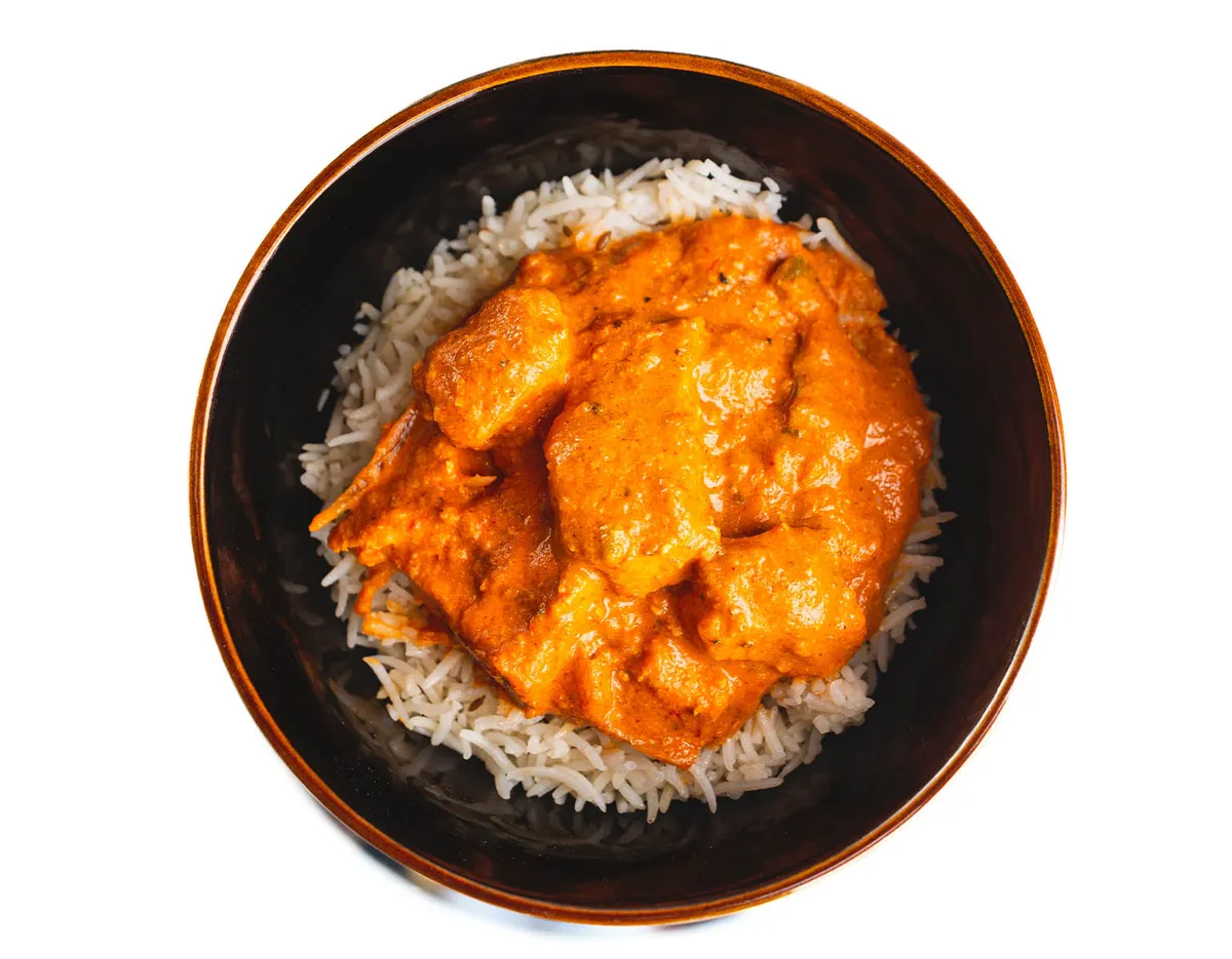 Orange curry with chunks of meat over white rice in a dark bowl