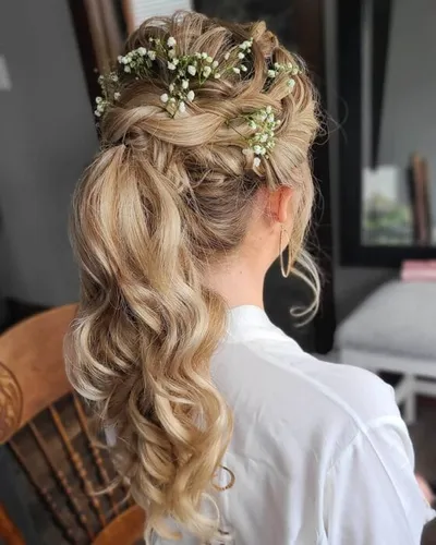 Woman's braided half-updo with baby's breath flowers and loose curled ponytail
