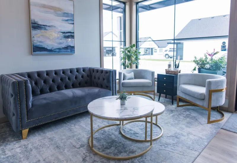 Gray tufted velvet sofa and light gray chairs around a marble-top gold coffee table in a modern lobby