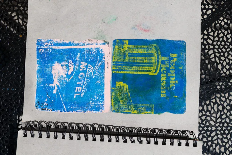 Two colorful monoprints in a spiral sketchbook — a blue motel sign and a yellow-blue building print