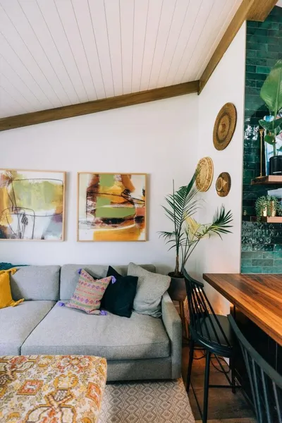Boho living room with gray sectional, colorful abstract art, palm plant, and teal tile accent wall