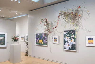 Art gallery wall with colorful floral paintings and a cascading botanical installation