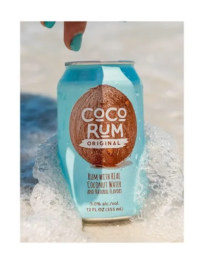 Hand holding a Coco Rum Original canned cocktail in ocean surf