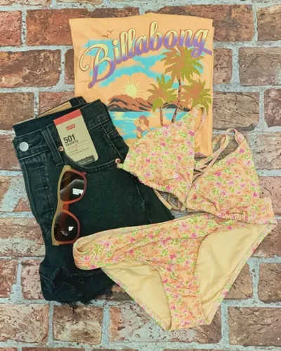 Billabong graphic tee, floral bikini, Levi's 501 cutoffs, and sunglasses on a brick surface