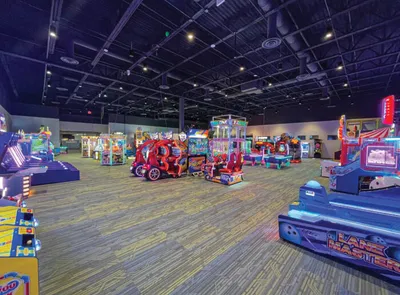 Spacious indoor arcade filled with colorful ride-on and ticket games under a black ceiling with track lighting