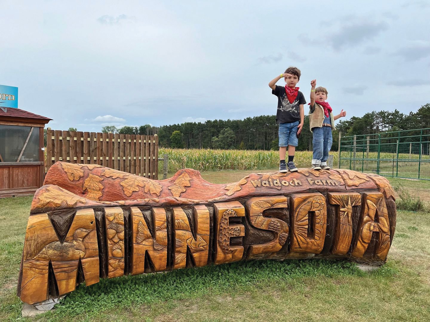 Two kids stand on a big carved wooden Minnesota sign at a farm
