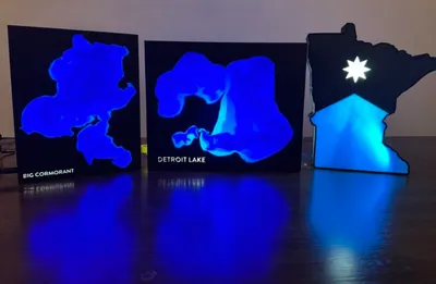 Three glowing blue lake map art pieces, labeled Big Cormorant and Detroit Lake, plus a Minnesota-shaped light