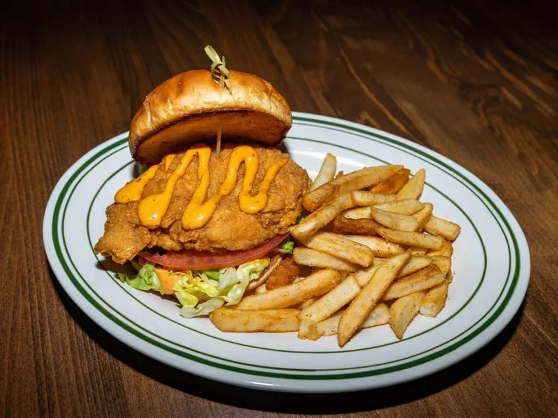 Crispy fried chicken sandwich with orange sauce and fries on a green-rimmed white plate