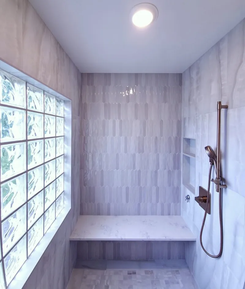 Walk-in shower with elongated hex tiles, built-in bench, bronze handheld showerhead, and glass block window