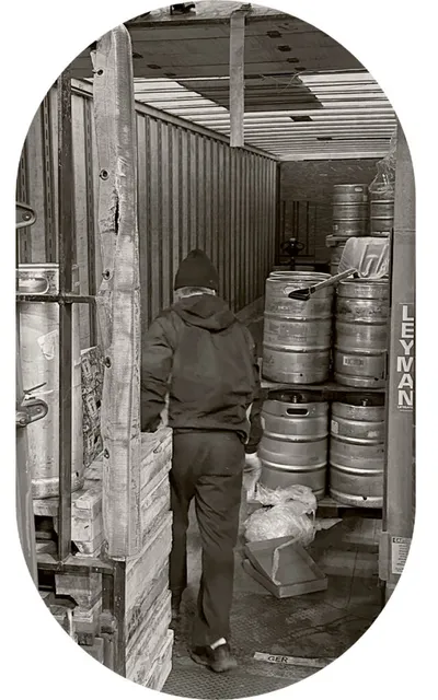 Worker in dark hoodie loading metal beer kegs into a delivery truck